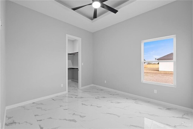 unfurnished bedroom featuring baseboards, a spacious closet, a ceiling fan, and marble finish floor