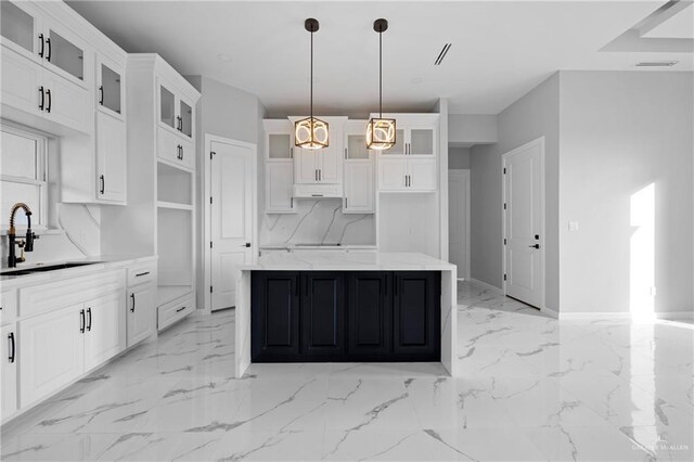 kitchen with under cabinet range hood, a kitchen island, marble finish floor, a sink, and white cabinetry