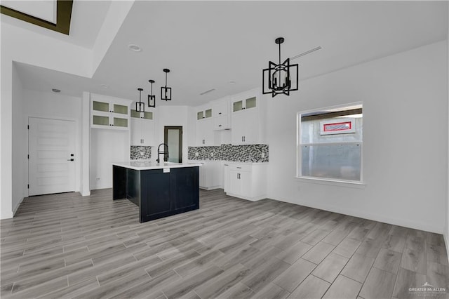 kitchen with backsplash, a kitchen island with sink, pendant lighting, light hardwood / wood-style floors, and white cabinetry