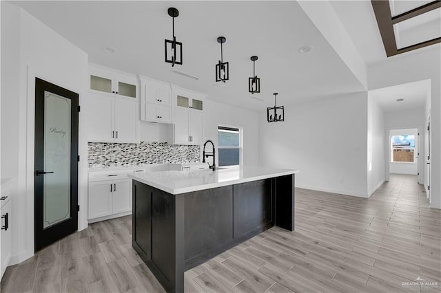 kitchen with white cabinets, decorative light fixtures, a kitchen island with sink, and a wealth of natural light