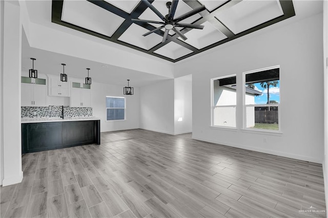 unfurnished living room featuring sink, ceiling fan with notable chandelier, light hardwood / wood-style floors, and coffered ceiling