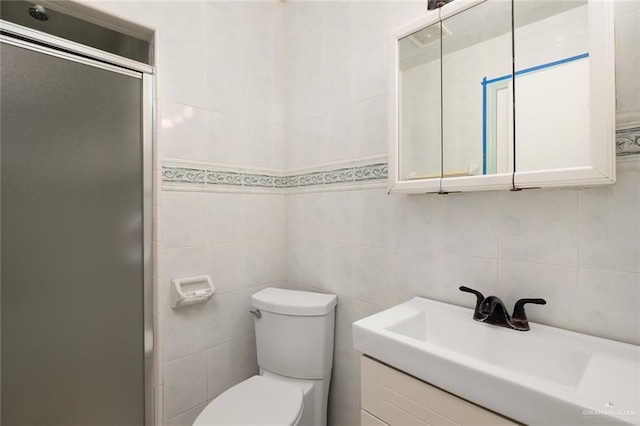 bathroom featuring vanity, toilet, a shower with shower door, and tile walls