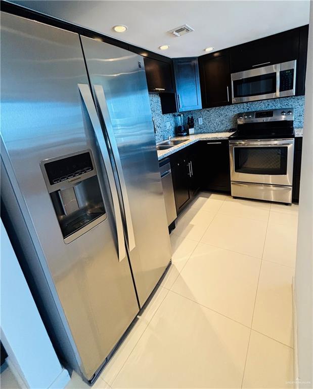 2100 Gulf Blvd, South Padre Island, TX 78597 - kitchen featuring appliances with stainless steel finishes, light countertops, light tile patterned floors, decorative backsplash, and dark cabinets