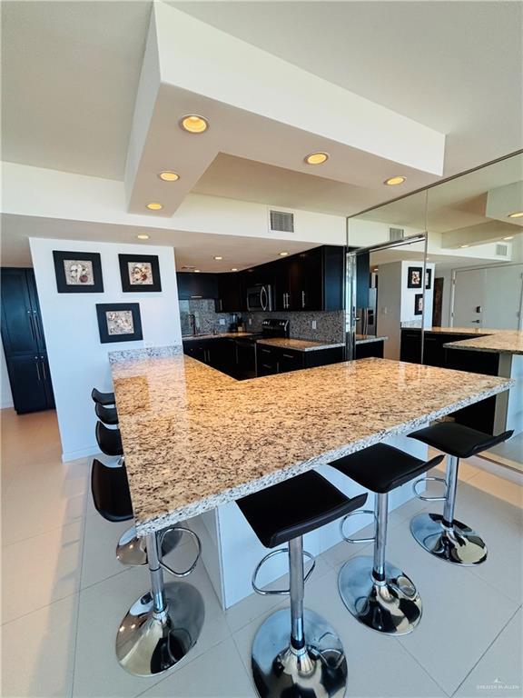 2100 Gulf Blvd, South Padre Island, TX 78597 - kitchen featuring a kitchen bar, stainless steel microwave, light stone counters, dark cabinets, and recessed lighting