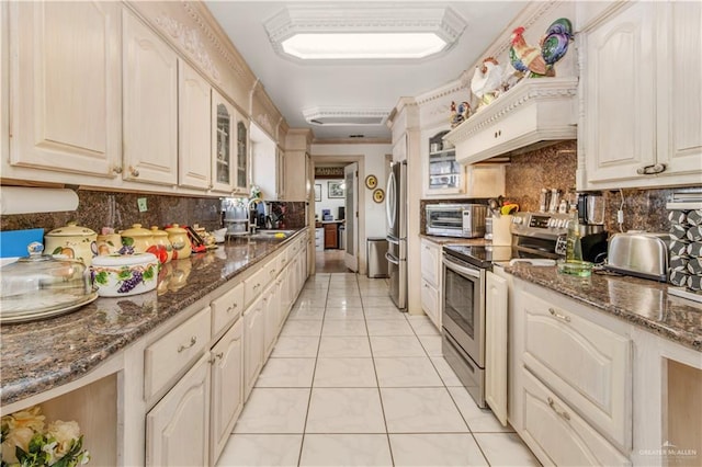 kitchen with appliances with stainless steel finishes, custom range hood, sink, light tile patterned floors, and dark stone countertops