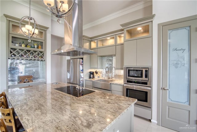 kitchen with island exhaust hood, light stone counters, stainless steel appliances, sink, and pendant lighting