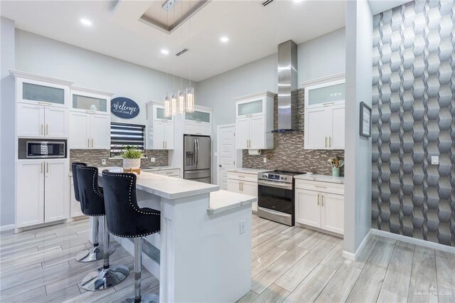 kitchen featuring pendant lighting, a center island, wall chimney exhaust hood, appliances with stainless steel finishes, and white cabinetry