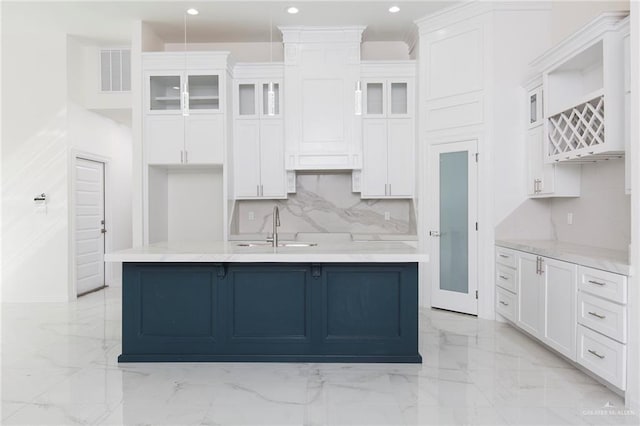 kitchen with sink, an island with sink, white cabinets, and backsplash