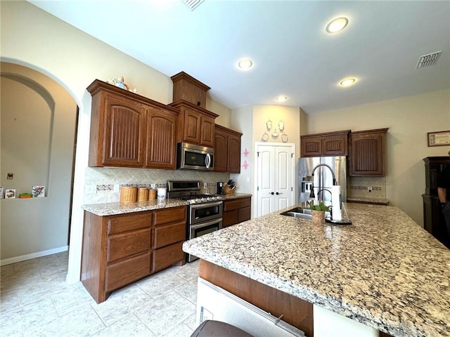 kitchen with decorative backsplash, light stone counters, sink, and appliances with stainless steel finishes