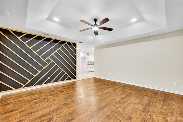 unfurnished room featuring ceiling fan, hardwood / wood-style flooring, and a tray ceiling