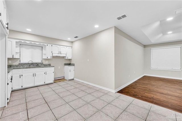 kitchen with stone counters, light tile patterned flooring, white cabinets, and sink