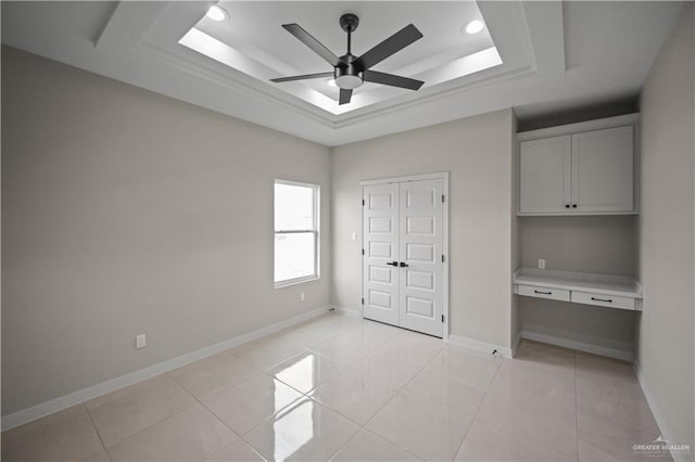 unfurnished bedroom featuring a raised ceiling, built in desk, baseboards, and light tile patterned floors