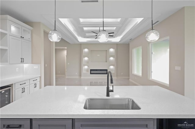 kitchen with a sink, open floor plan, open shelves, a tray ceiling, and a center island with sink