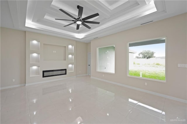 unfurnished living room with light tile patterned floors, baseboards, a raised ceiling, and a glass covered fireplace