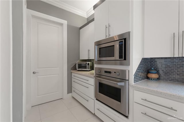 kitchen featuring crown molding, white cabinetry, tasteful backsplash, light tile patterned floors, and stainless steel appliances