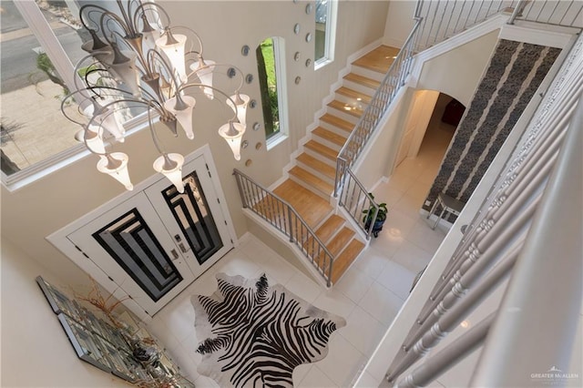 staircase with arched walkways, tile patterned flooring, a towering ceiling, and a chandelier
