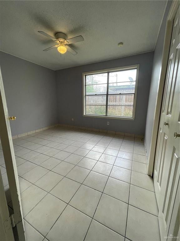 unfurnished room featuring light tile patterned floors, a textured ceiling, baseboards, and a ceiling fan