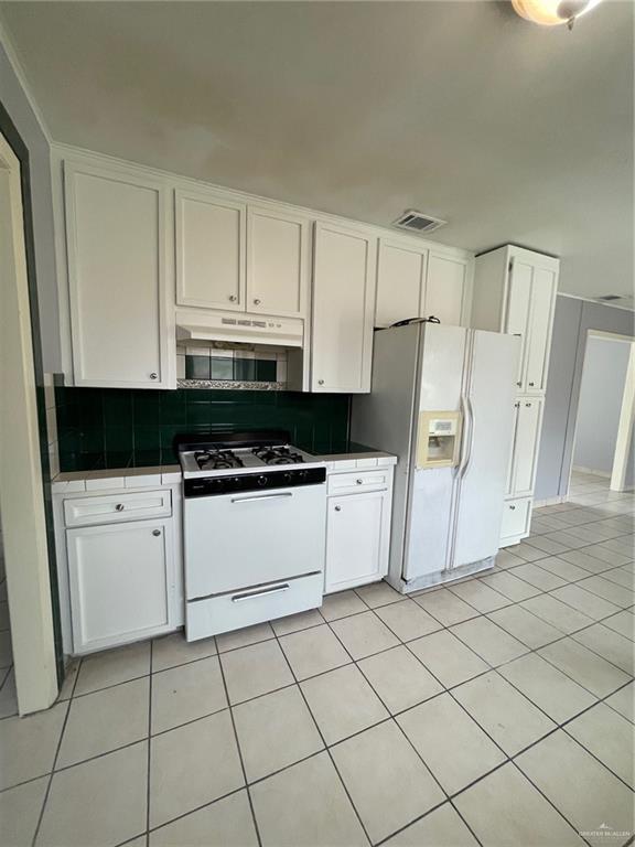 kitchen with tile countertops, tasteful backsplash, white cabinetry, white appliances, and under cabinet range hood