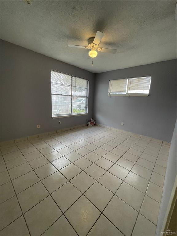 tiled empty room featuring ceiling fan and a textured ceiling