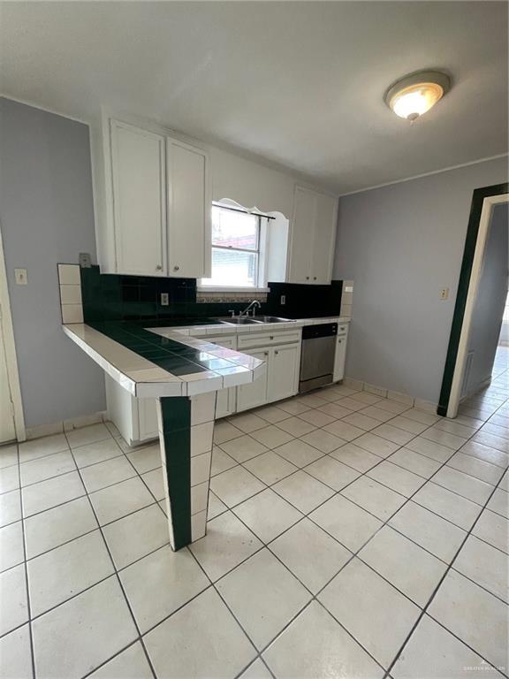 kitchen with light tile patterned floors, tile counters, white cabinets, dishwasher, and a peninsula