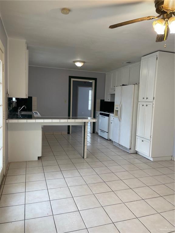 kitchen featuring light tile patterned floors, tile counters, white cabinets, white appliances, and a peninsula