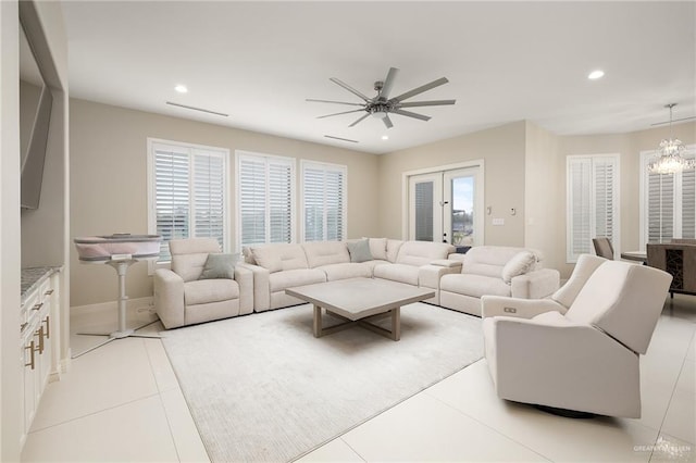 tiled living room with ceiling fan with notable chandelier and french doors