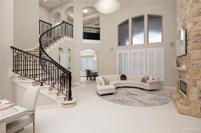 tiled living room with a stone fireplace, a high ceiling, and a notable chandelier