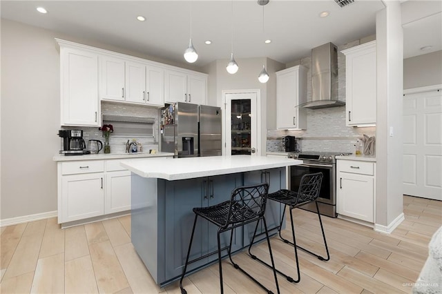 kitchen featuring wall chimney range hood, a kitchen island, pendant lighting, stainless steel appliances, and white cabinets