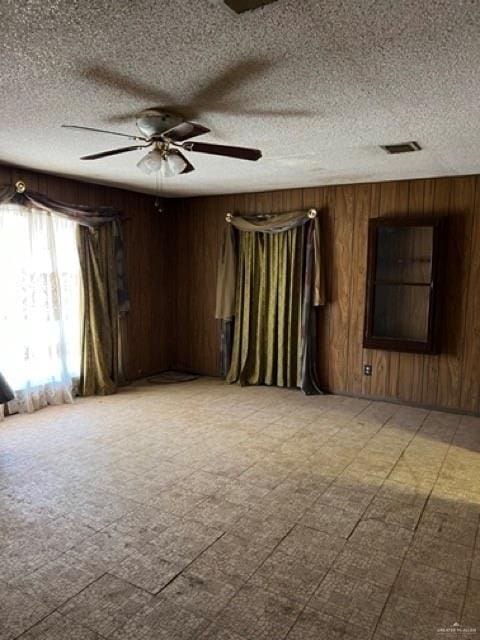 spare room featuring a textured ceiling, ceiling fan, and wooden walls