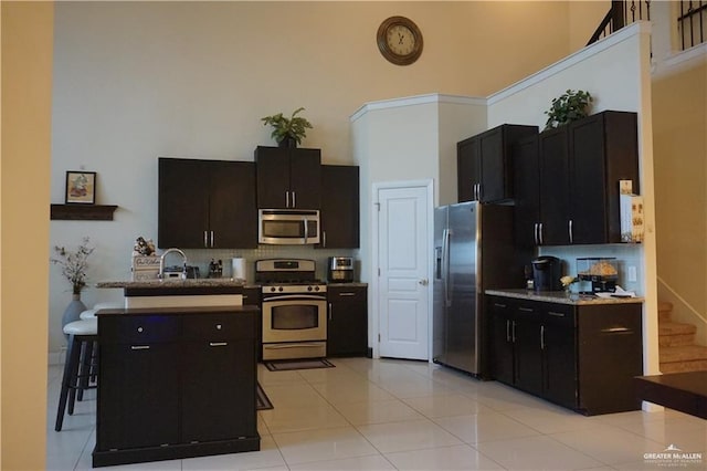 kitchen featuring sink, a towering ceiling, decorative backsplash, light tile patterned floors, and appliances with stainless steel finishes