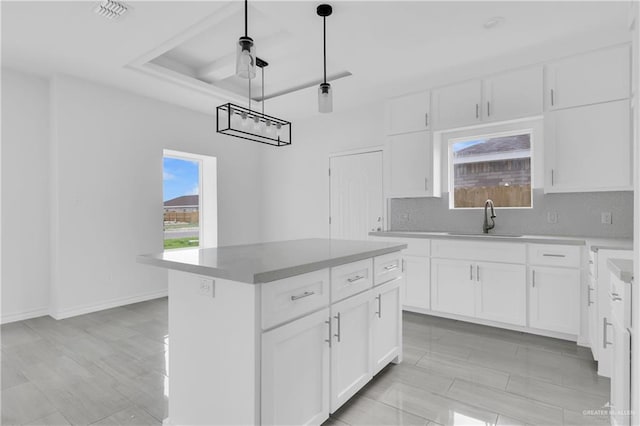 kitchen featuring backsplash, sink, decorative light fixtures, white cabinets, and a center island