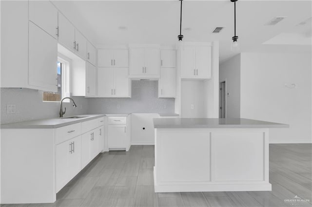 kitchen with white cabinets, a center island, hanging light fixtures, and sink