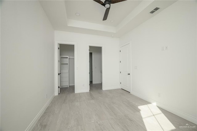 unfurnished bedroom with a raised ceiling, a closet, a spacious closet, and ceiling fan