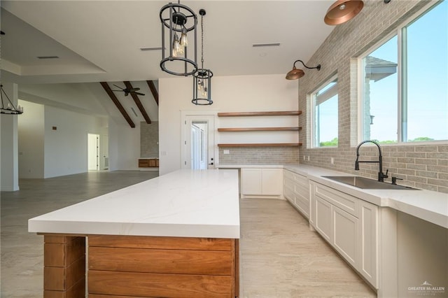 kitchen featuring pendant lighting, sink, tasteful backsplash, a kitchen island, and white cabinetry