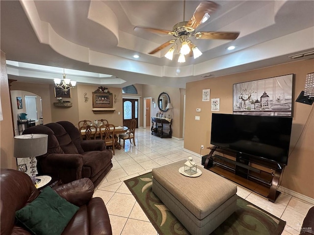 living room with ceiling fan with notable chandelier, a raised ceiling, and light tile patterned floors