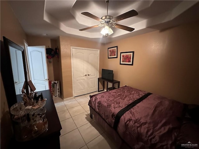 bedroom featuring light tile patterned floors, a closet, a raised ceiling, and ceiling fan