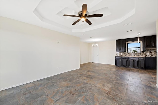 unfurnished living room featuring sink, a tray ceiling, and ceiling fan with notable chandelier