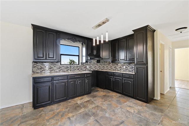 kitchen featuring hanging light fixtures, light stone countertops, sink, and backsplash