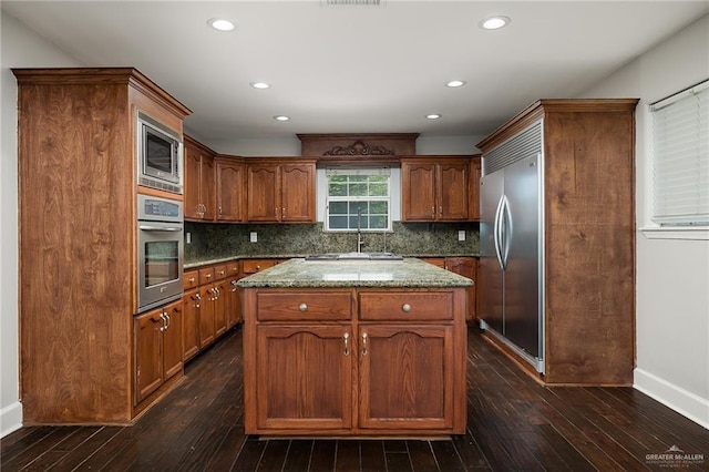 kitchen with tasteful backsplash, dark wood-style flooring, a center island, built in appliances, and stone counters