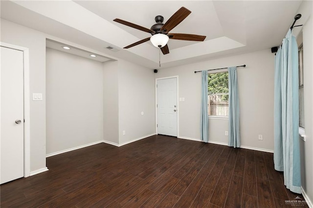 empty room featuring a tray ceiling, wood finished floors, visible vents, and baseboards