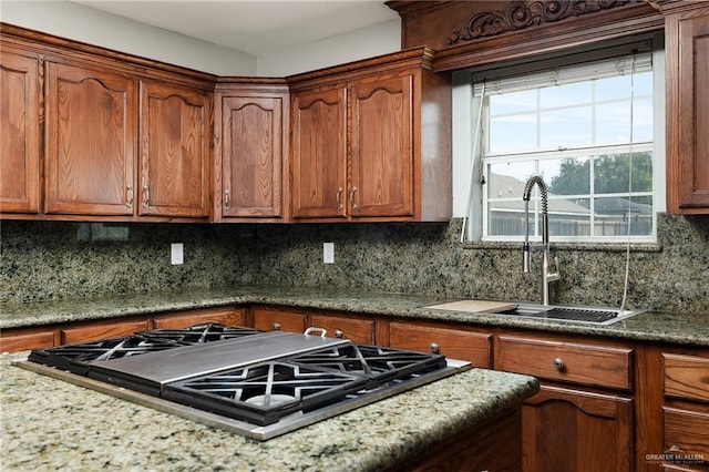 kitchen featuring tasteful backsplash, brown cabinetry, stovetop, and a sink