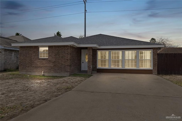 single story home featuring brick siding, fence, and roof with shingles