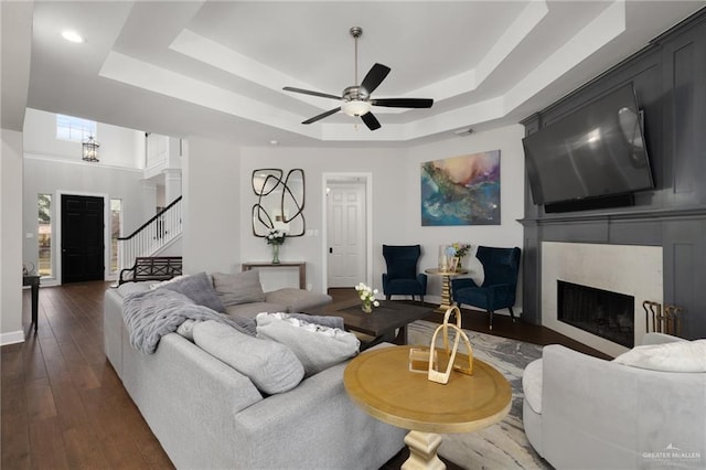 living room with ceiling fan, dark wood-type flooring, a premium fireplace, stairs, and a raised ceiling