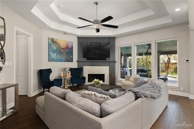 living area with dark wood-type flooring, a fireplace, a raised ceiling, and baseboards