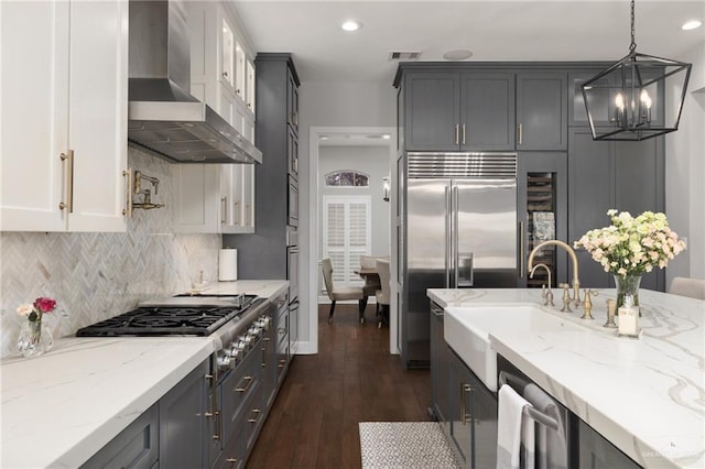 kitchen with visible vents, light stone countertops, stainless steel appliances, wall chimney range hood, and a sink