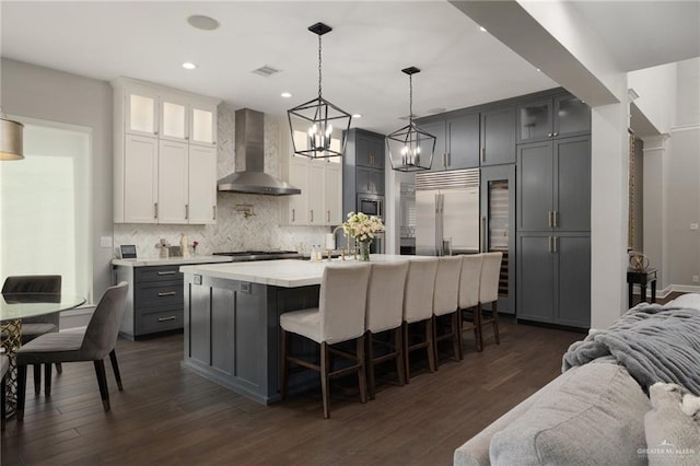 kitchen with visible vents, open floor plan, built in appliances, light countertops, and wall chimney range hood