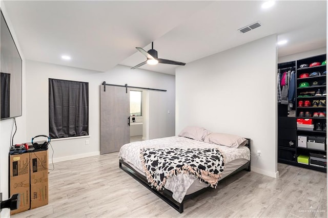 bedroom featuring ceiling fan, a barn door, light hardwood / wood-style floors, and a closet