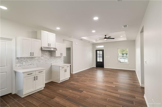 kitchen featuring ceiling fan, dark hardwood / wood-style floors, backsplash, a tray ceiling, and white cabinets