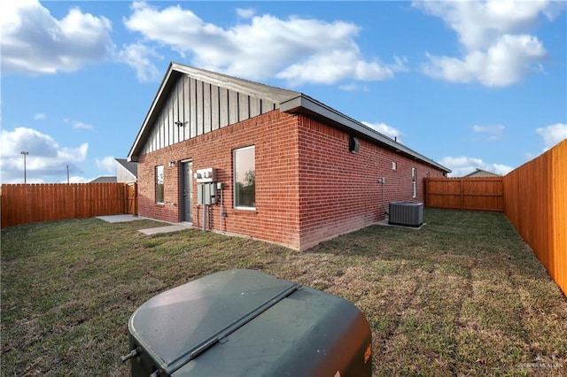 view of side of property featuring brick siding, a yard, central air condition unit, board and batten siding, and a fenced backyard