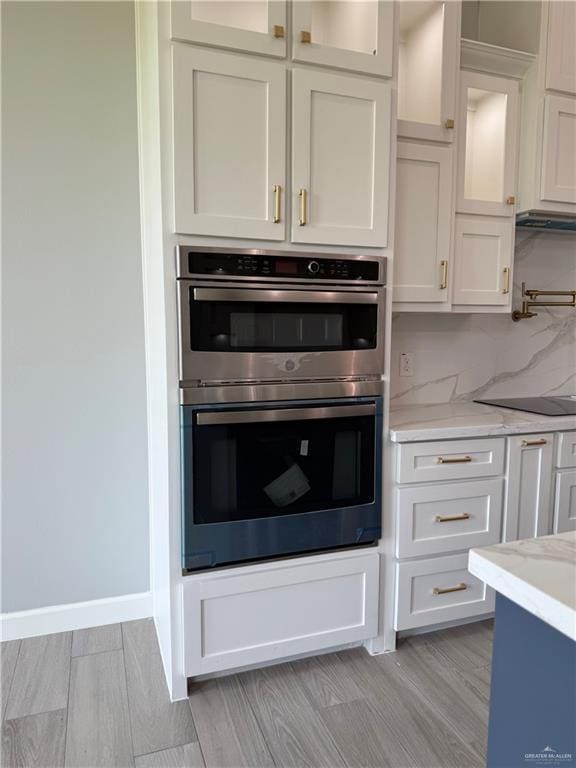1203 Moses Dr, San Juan, TX 78589 - kitchen with decorative backsplash, white cabinets, glass insert cabinets, double oven, and light stone counters